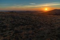 there is a sunset in the horizon on a field with grassy land below the mountains