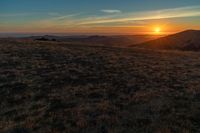 there is a sunset in the horizon on a field with grassy land below the mountains