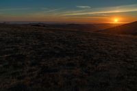 there is a sunset in the horizon on a field with grassy land below the mountains