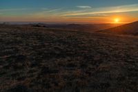 there is a sunset in the horizon on a field with grassy land below the mountains