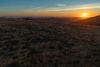 there is a sunset in the horizon on a field with grassy land below the mountains