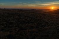 there is a sunset in the horizon on a field with grassy land below the mountains