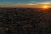 there is a sunset in the horizon on a field with grassy land below the mountains