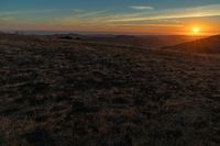 there is a sunset in the horizon on a field with grassy land below the mountains