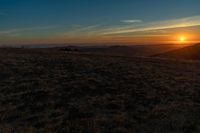 there is a sunset in the horizon on a field with grassy land below the mountains