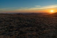 there is a sunset in the horizon on a field with grassy land below the mountains