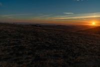 there is a sunset in the horizon on a field with grassy land below the mountains