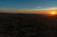 there is a sunset in the horizon on a field with grassy land below the mountains