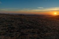 there is a sunset in the horizon on a field with grassy land below the mountains