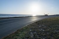 an empty road near a beach and waves as well as cars on the sand and houses on the beach