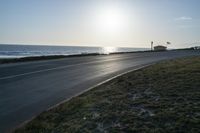 an empty road near a beach and waves as well as cars on the sand and houses on the beach