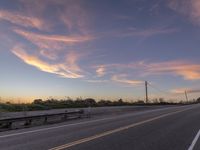 a highway with trees, bushes and a sky with white clouds at sunset at the end