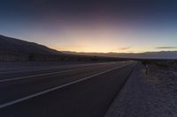 a view of a sun setting over a highway in the desert with a sign in the middle