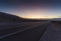 a view of a sun setting over a highway in the desert with a sign in the middle