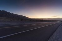 a view of a sun setting over a highway in the desert with a sign in the middle