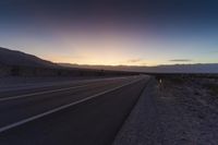 a view of a sun setting over a highway in the desert with a sign in the middle