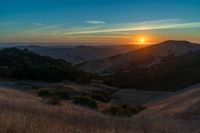 there is a sunset in the horizon on a field with grassy land below the mountains