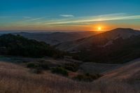 there is a sunset in the horizon on a field with grassy land below the mountains