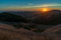 there is a sunset in the horizon on a field with grassy land below the mountains