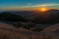 there is a sunset in the horizon on a field with grassy land below the mountains