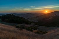 there is a sunset in the horizon on a field with grassy land below the mountains