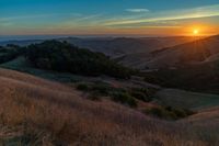 there is a sunset in the horizon on a field with grassy land below the mountains