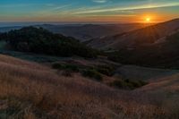 there is a sunset in the horizon on a field with grassy land below the mountains