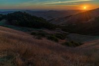 there is a sunset in the horizon on a field with grassy land below the mountains