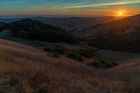 there is a sunset in the horizon on a field with grassy land below the mountains