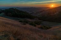 there is a sunset in the horizon on a field with grassy land below the mountains