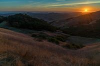 there is a sunset in the horizon on a field with grassy land below the mountains