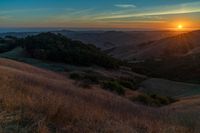 there is a sunset in the horizon on a field with grassy land below the mountains