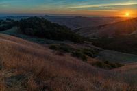 there is a sunset in the horizon on a field with grassy land below the mountains