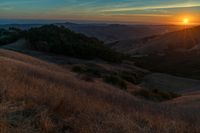 there is a sunset in the horizon on a field with grassy land below the mountains