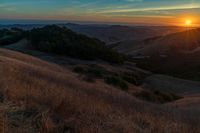 there is a sunset in the horizon on a field with grassy land below the mountains