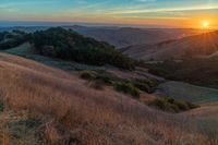 there is a sunset in the horizon on a field with grassy land below the mountains