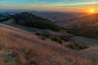 there is a sunset in the horizon on a field with grassy land below the mountains