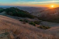 there is a sunset in the horizon on a field with grassy land below the mountains