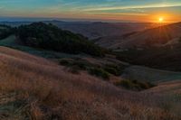 there is a sunset in the horizon on a field with grassy land below the mountains