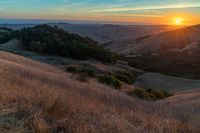 there is a sunset in the horizon on a field with grassy land below the mountains