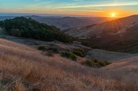 there is a sunset in the horizon on a field with grassy land below the mountains