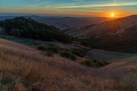 there is a sunset in the horizon on a field with grassy land below the mountains