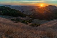 there is a sunset in the horizon on a field with grassy land below the mountains