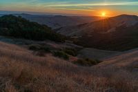 there is a sunset in the horizon on a field with grassy land below the mountains