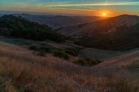 there is a sunset in the horizon on a field with grassy land below the mountains