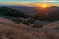 there is a sunset in the horizon on a field with grassy land below the mountains