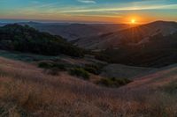 there is a sunset in the horizon on a field with grassy land below the mountains