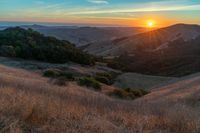 there is a sunset in the horizon on a field with grassy land below the mountains