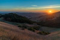 there is a sunset in the horizon on a field with grassy land below the mountains