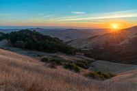 there is a sunset in the horizon on a field with grassy land below the mountains